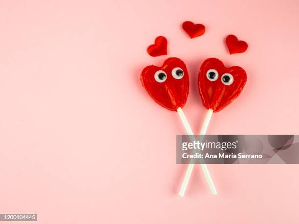 concept of love and romanticism. two red heart lollipops with eyes looking at each other and several red hearts - love at first sight stock-fotos und bilder