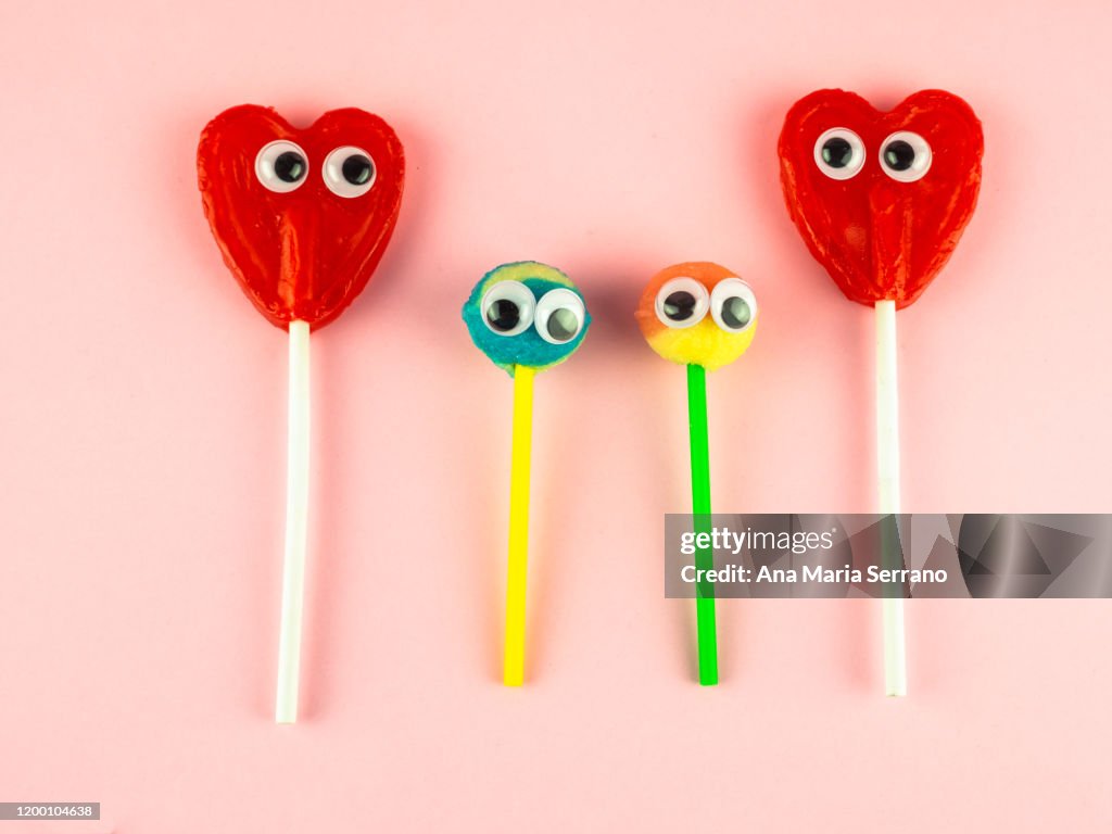 Concept of love and family. Two red heart lollipops with eyes looking at each other and two smaller lollipops