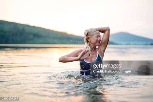 active senior woman standing in water in lake outdoors in nature. copy space. - old woman in swimsuit imagens e fotografias de stock