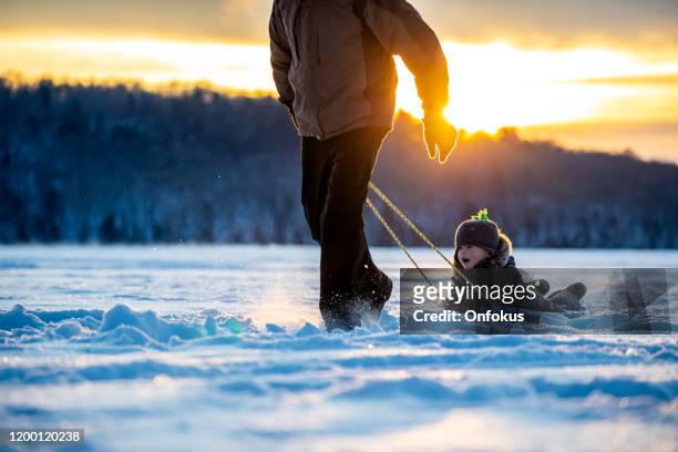 grandfather pulling grandson on sled on frozen lake in winter at sunset - recreational equipment stock pictures, royalty-free photos & images