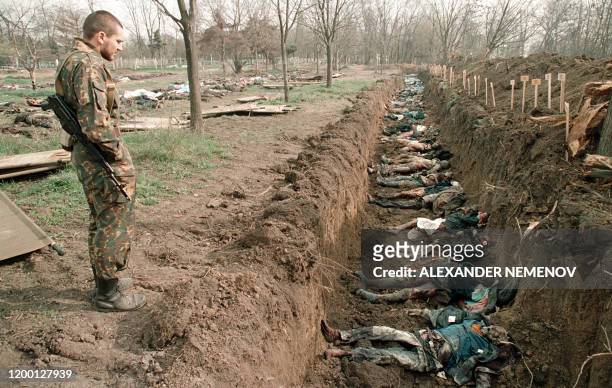 Picture taken on March 31, 1995 shows a Russian soldier inspecting the bodies of civilans killed in winter fighting that have been exhumed for...