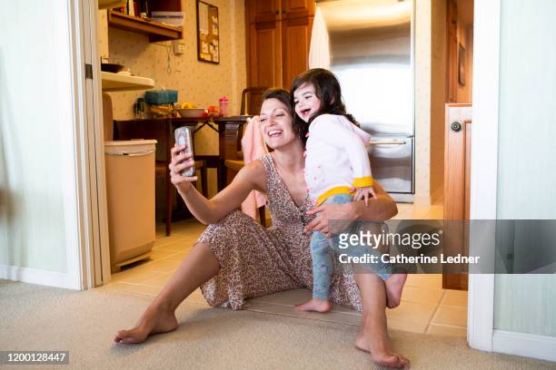 Mother and daughter laughing and smiling while face timing on kitchen floor