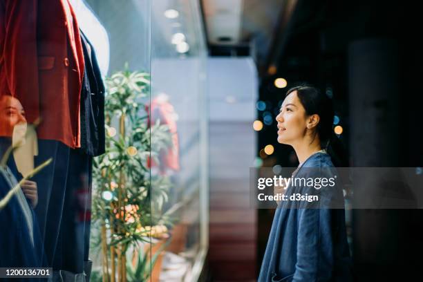 young asian woman looking at shop window while walking in the city at night - boutique ストックフォトと画像