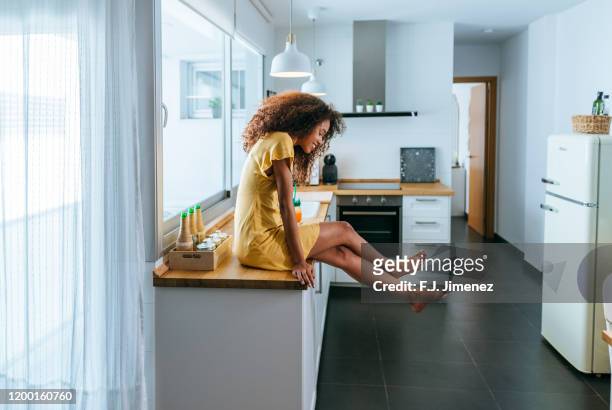 relaxed woman sitting on the kitchen counter - yellow dress stock pictures, royalty-free photos & images