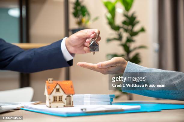 estate agent giving house keys to woman and sign agreement in office - kaufen stock-fotos und bilder