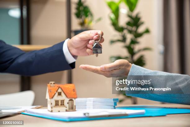 estate agent giving house keys to woman and sign agreement in office - huurhuis stockfoto's en -beelden