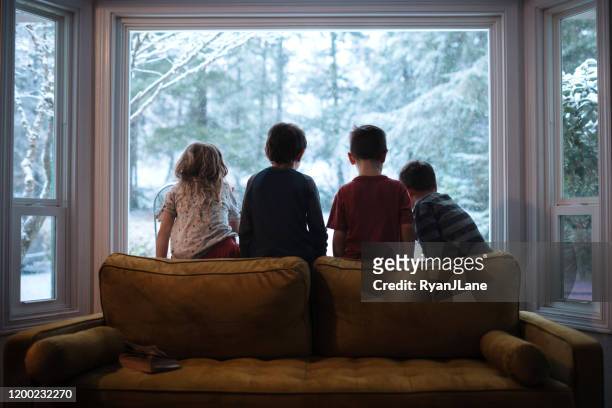 kinder, die bei fallendem schnee aus dem fenster schauen - winter stock-fotos und bilder