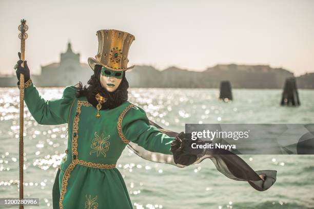 persona enmascarada en traje de carnaval verde con sombrero de oro posando cerca de canale grande, venecia - carnaval de venecia fotografías e imágenes de stock