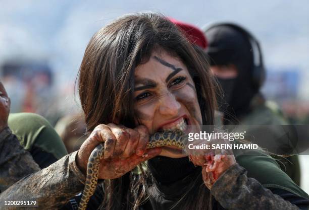 An Iraqi Kurdish Peshmerga female officer bites a snake while demonstrating skills during a graduation ceremony in the Kurdish town of Soran, about...