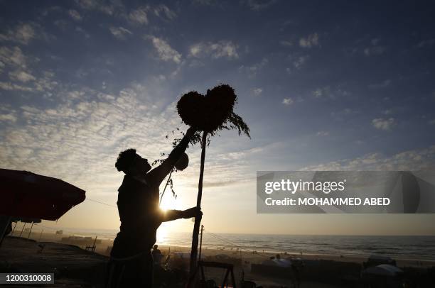 Palestinian youth silhoueted on the coast of Gaza city places a decorative heart on a pole on the beach ahead of Valentine's Day in the Hamas-run...