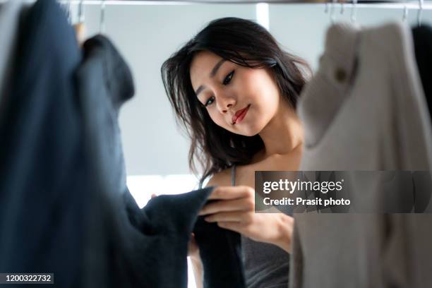 asian happy young woman choosing  winter clothes hanging in rail in mall or clothing store. shopaholic people, retail special offer price, holiday vacation activity lifestyle concept. - rack stock pictures, royalty-free photos & images