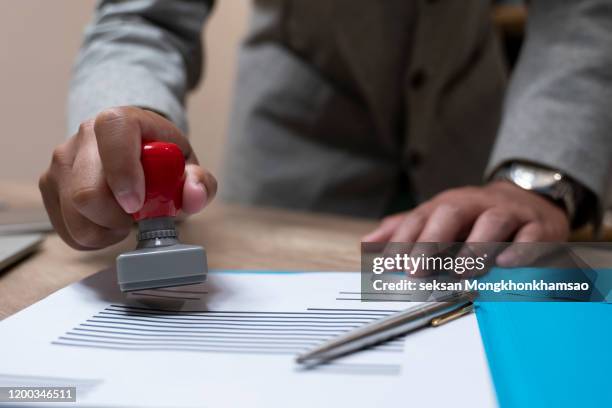 close-up of a person's hand stamping with approved stamp on document at desk - notar stock-fotos und bilder