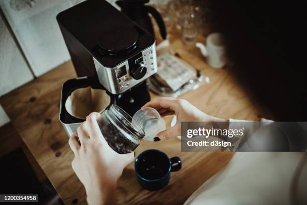 young woman measuring and pouring roasted coffee beans into coffee machine and preparing coffee at home in the early morning - 焙煎 ストックフォトと画像