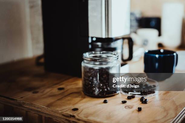 a morning coffee setting with roasted coffee beans, coffee cup and coffee machine in the kitchen counter - coffee machine home stock pictures, royalty-free photos & images