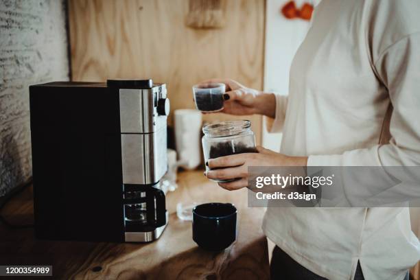 young woman measuring and pouring roasted coffee beans into coffee machine and preparing coffee at home in the early morning - grinder stock-fotos und bilder