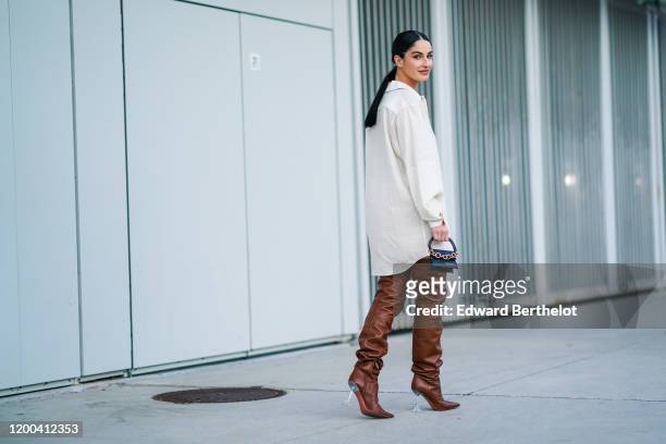 Fiona Zanetti wears a white ling shirt, a Jacquemus mini bag with a golden chain, brown leather thigh high pointy boots, outside Jacquemus, during...