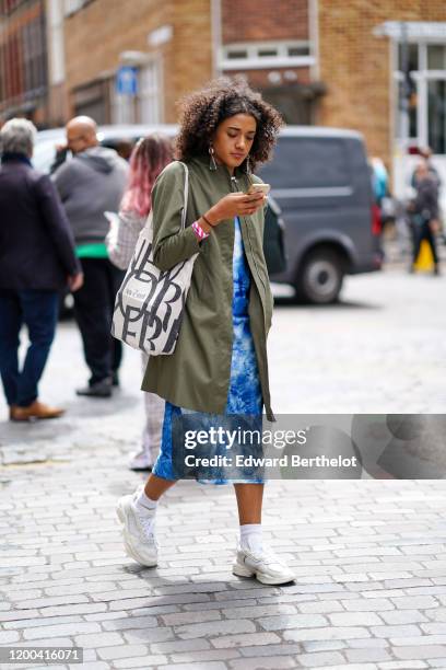 Guest wears earrings, a khaki trench coat, a white New Yorker tote bag, a marble-effect blue and white dress, white ankle-socks, white sneakers,...