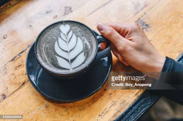 cropped shot view of someone hand touching a cup of goth latte or charcoal latte on wooden table. - goth boy stock-fotos und bilder