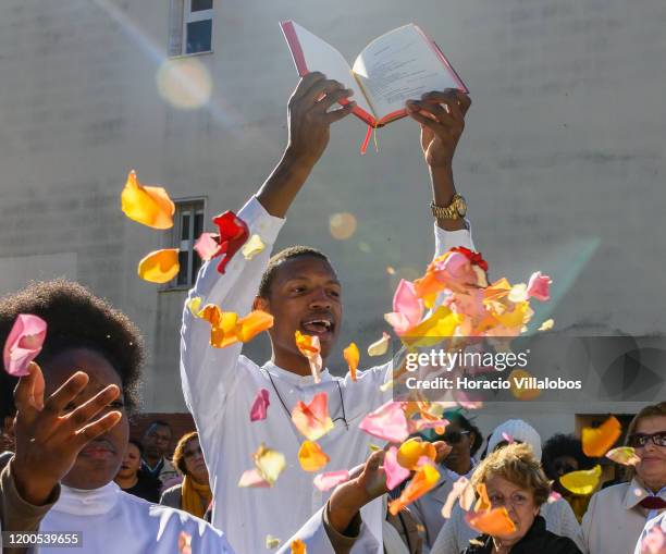 Faithful hold the bible above their heads while chanting and throwing rose petals during an outdoors mass, part of the Festivities of Santo Amaro, a...