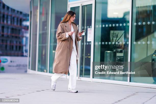 Guest wears a light brown wool coat, a white jacket, white pants, light grey sneakers, outside Jacquemus, during Paris Fashion Week - Menswear F/W...