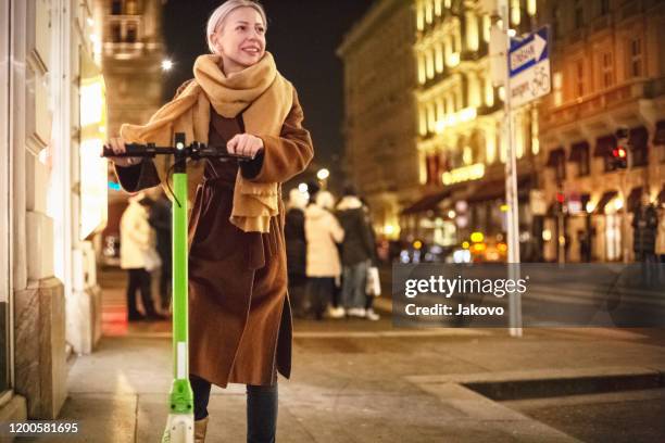 woman using electric scooter and checking her smartphone - motor scooter night stock pictures, royalty-free photos & images