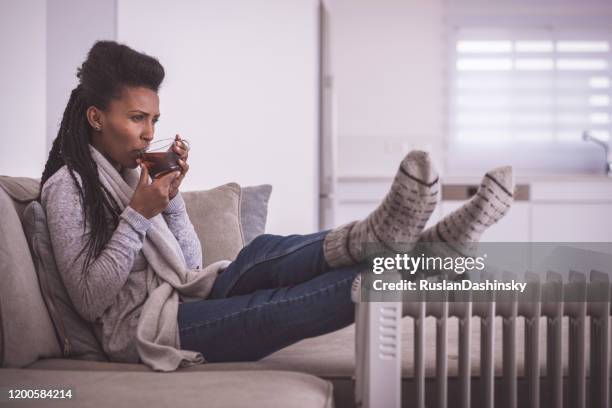 mujer bebiendo té caliente, calentando los pies en casa. - electric heater fotografías e imágenes de stock