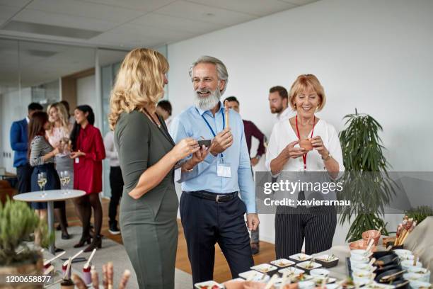 hungry colleagues sampling gourmet small dishes at party - office party stock pictures, royalty-free photos & images