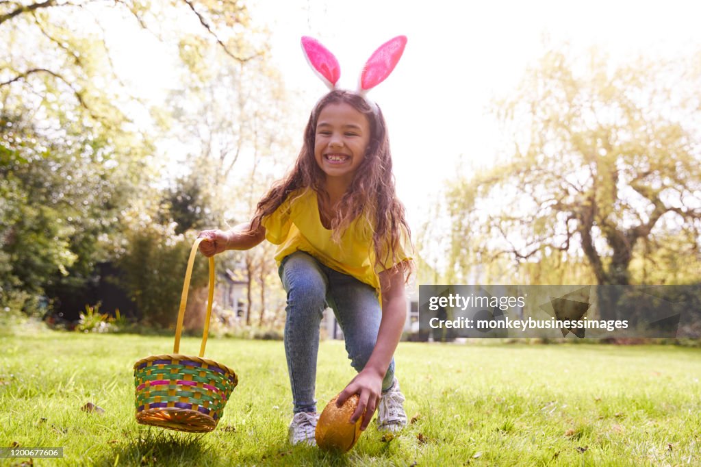 Portret van meisje dragen bunny oren vinden van chocolade ei op Easter Egg Hunt in de tuin