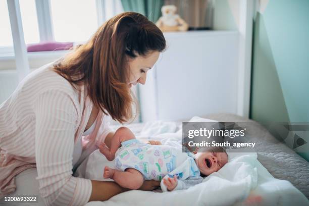 madre che cambia pannolino sul suo bambino a letto in camera da letto - adult baby boy diaper change foto e immagini stock