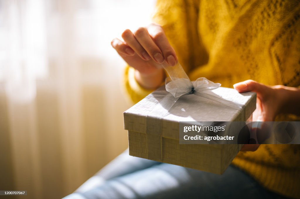 Young woman in yellow sweater opening gift box