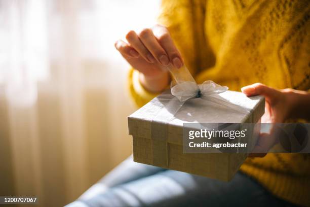 young woman in yellow sweater opening gift box - giving imagens e fotografias de stock