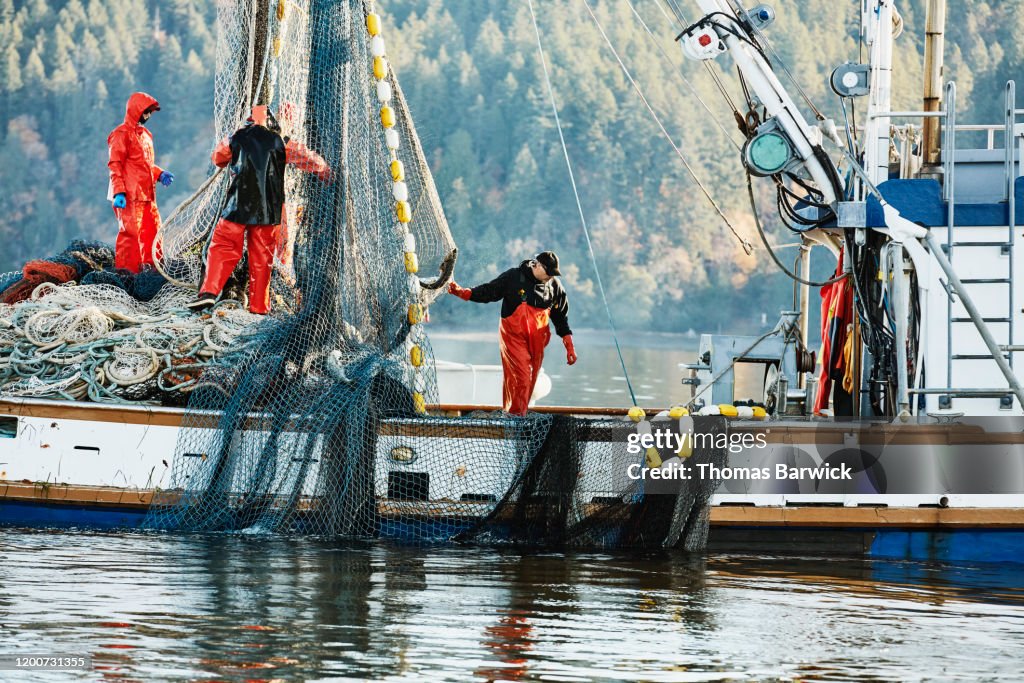 Crew of fishing boat hauling in net while fishing for salmon
