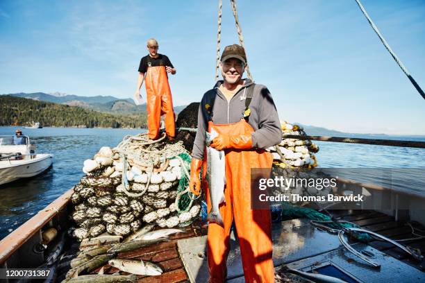 portrait of captain of purse seiner holding coho salmon - bateau de pêche photos et images de collection