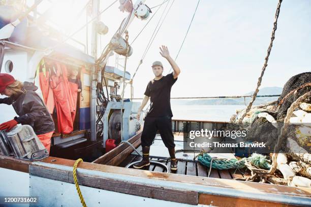 crew member of fishing boat waving from stern deck of boat - value chain stock pictures, royalty-free photos & images