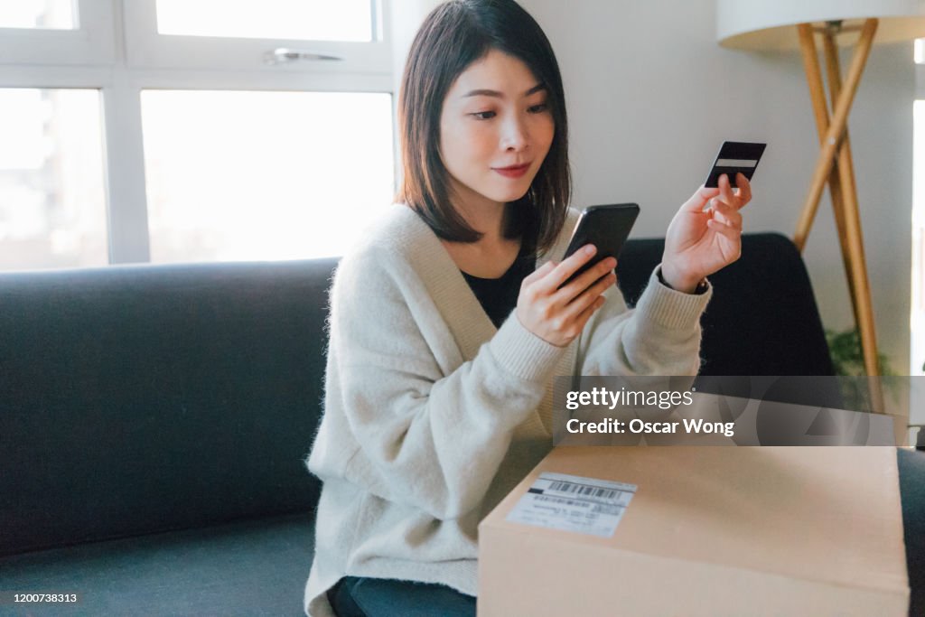 Woman shopping online with mobile phone and credit card at home