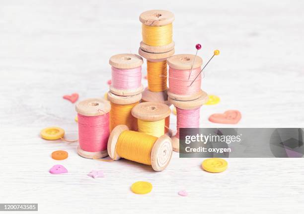 collection of spools threads pins in yellow pink colors arranged on a white wooden background - button sewing item stock-fotos und bilder
