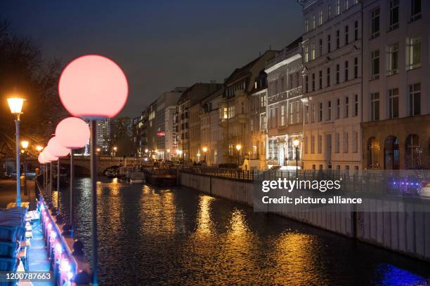 February 2020, Berlin: The red glowing lights of a restaurant on the Fischerinsel on the Roßstraßenbrücke line the bank of the Spreekanal. On the...