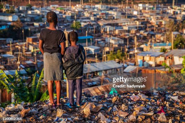 niñas africanas de pie en la basura y mirando a la barriada de kibera, kenia, - kenia fotografías e imágenes de stock
