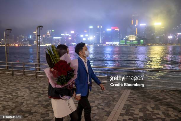 People wearing protective face masks walk along a promenade with a flower bouquet at night in the Tsim Sha Tsui district of Hong Kong, China, on...
