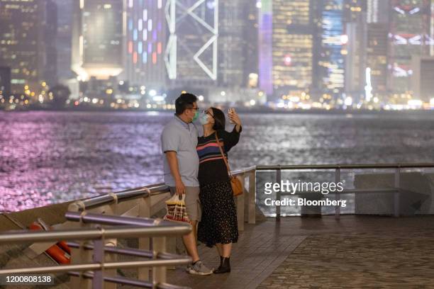 People wearing protective face masks pose for a selfie photograph against the city skyline at night in the Tsim Sha Tsui district of Hong Kong,...
