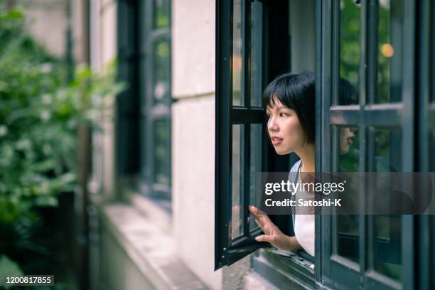 ung kvinna öppnar fönstret och tittar på utsikten - open city bildbanksfoton och bilder