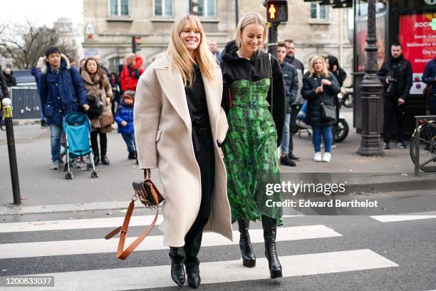 Jeanette Madsen wears a black top, a cream-color oversized wool coat, a black and tan-color bag, black pointy boots ; Thora Valdimars wears a black...