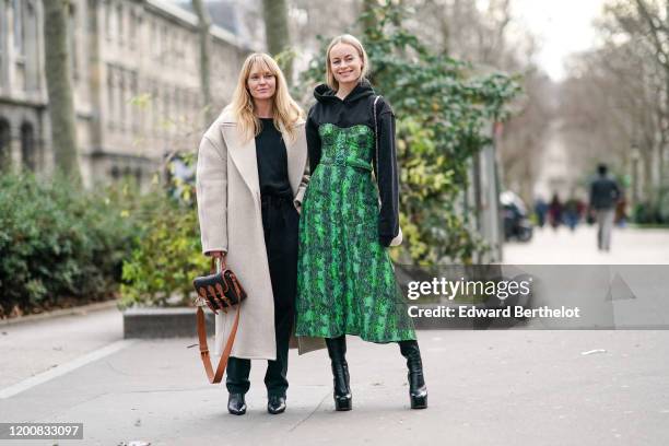 Jeanette Madsen wears a black top, a cream-color oversized wool coat, a black and tan-color bag, black boots ; Thora Valdimars wears a black hooded...