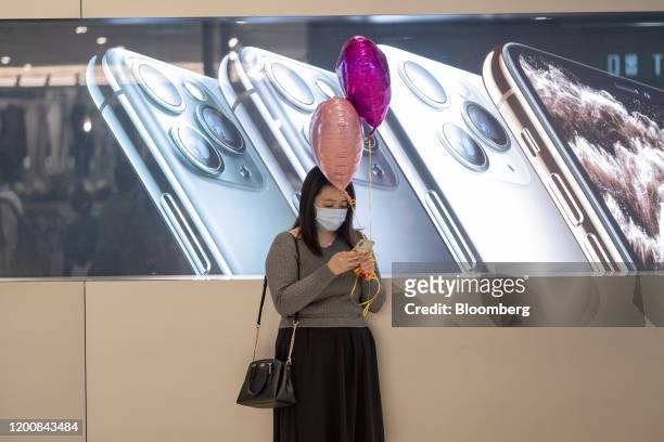 Woman wearing a protective mask uses a smartphone while holding balloons in front of an advertisement for Apple Inc. IPhone in Hong Kong, China, on...