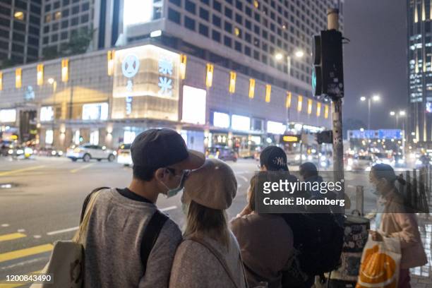 People wearing protective masks share a moment while waiting at a pedestrian crossing at night in the Tsim Sha Tsui district of Hong Kong, China, on...