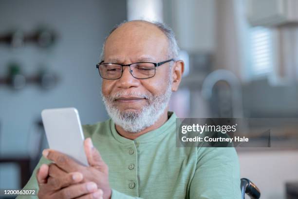 senior männlich trägt brille verwendet handy in der häuslichen küche - male cellphone stock-fotos und bilder
