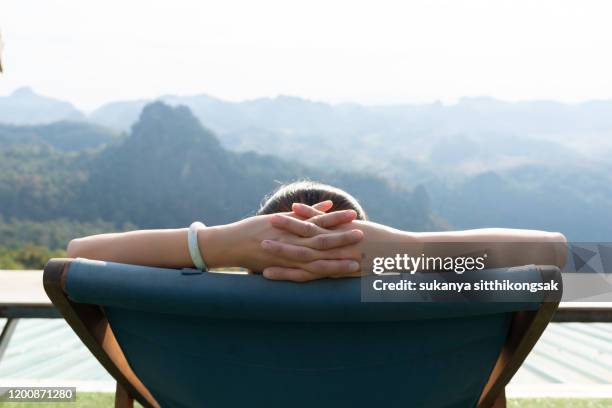 close up young woman slepping while relaxing on deck chair and looking at nature, with mountains in the background. - sitting back foto e immagini stock