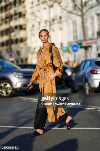 Lauren Santo Domingo wears a camel flowing long trench coat, a black bag, black pants, black flat mules, outside Dior, during Paris Fashion Week -...