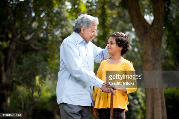 happy girl holding hands of grandfather at park - respect stock pictures, royalty-free photos & images