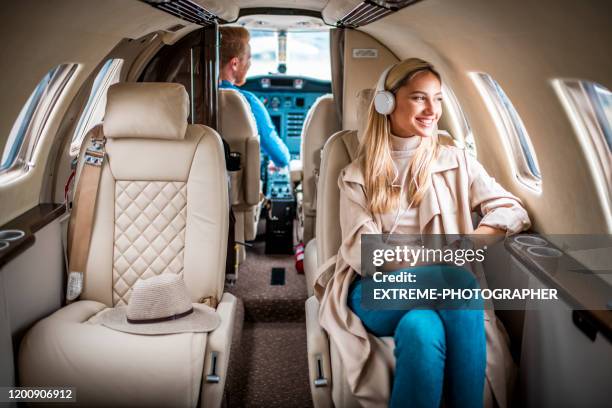 joven, mujer rubia de moda disfrutando de la música sobre los auriculares mientras vuela a bordo de un jet privado - cabina interior del vehículo fotografías e imágenes de stock